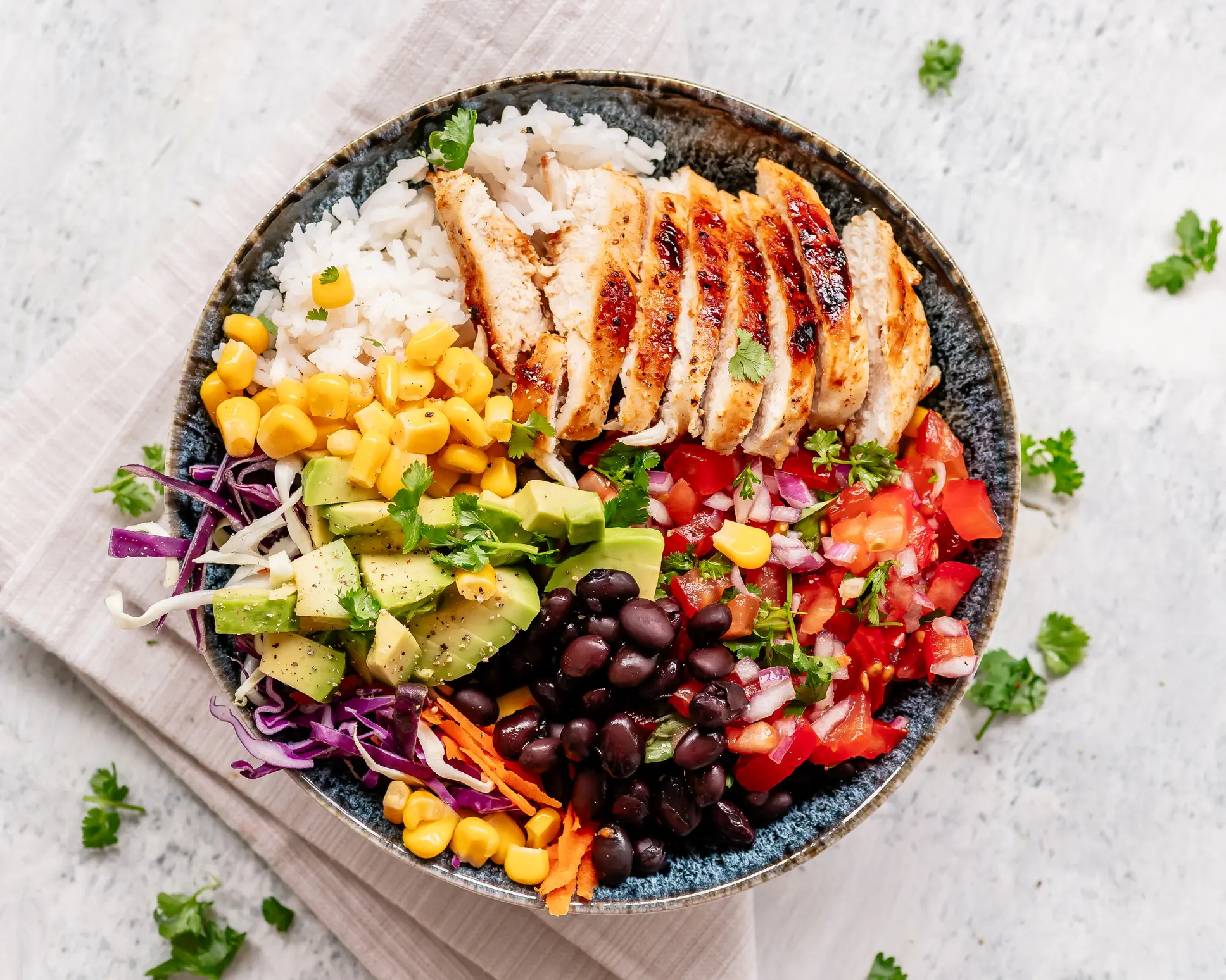 Mexican style healthy bowl with rice, grilled chicken breast, tomato salsa, black beans, corn, avocado and veggies