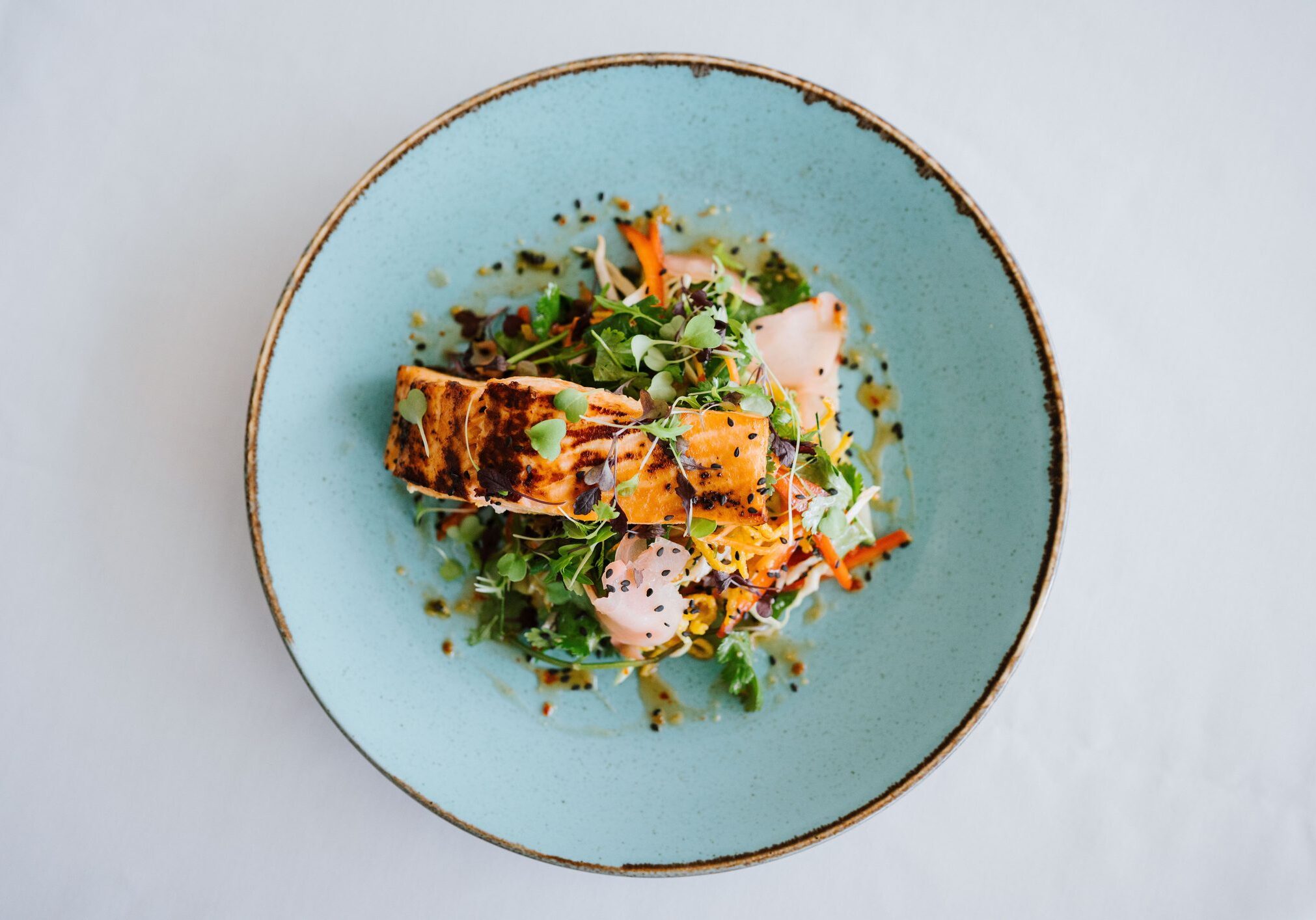 A gourmet dish of grilled salmon with fresh greens and vegetables served on a blue plate.